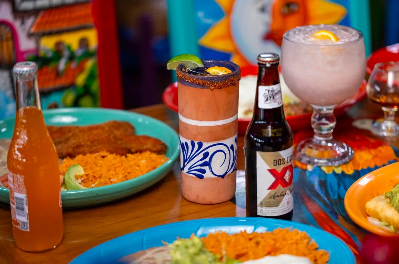 Margaritas, a Dos Equis and an orange Jarritos on a table by the colourful murals
