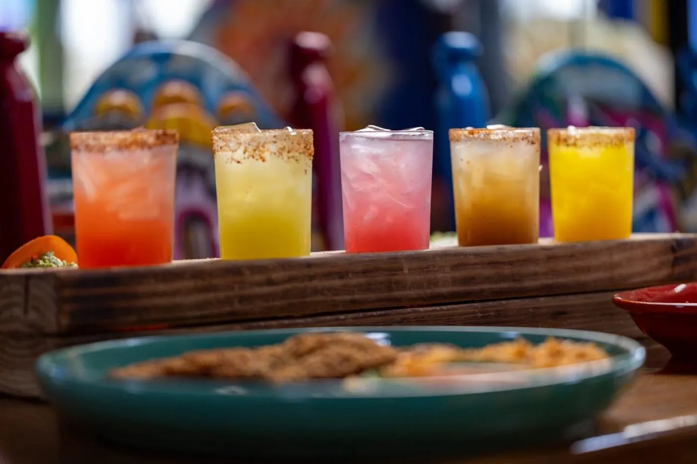 Five margaritas in a row on a wooden board, red, yellow, pink, amber and orange