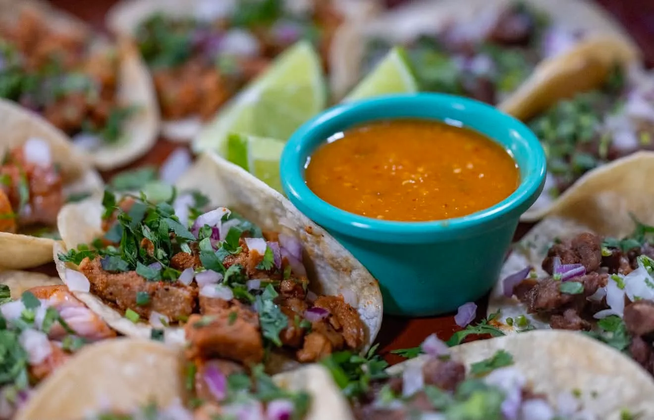 Street tacos heaped with meat, cilantro and onion around a bowl of salsa and lime wedges